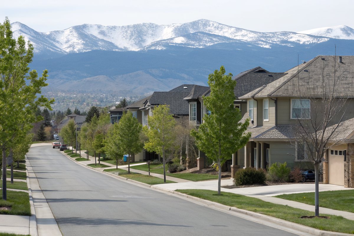 A quiet street of two-story homes with gray shingle roofs, mountains in the distance